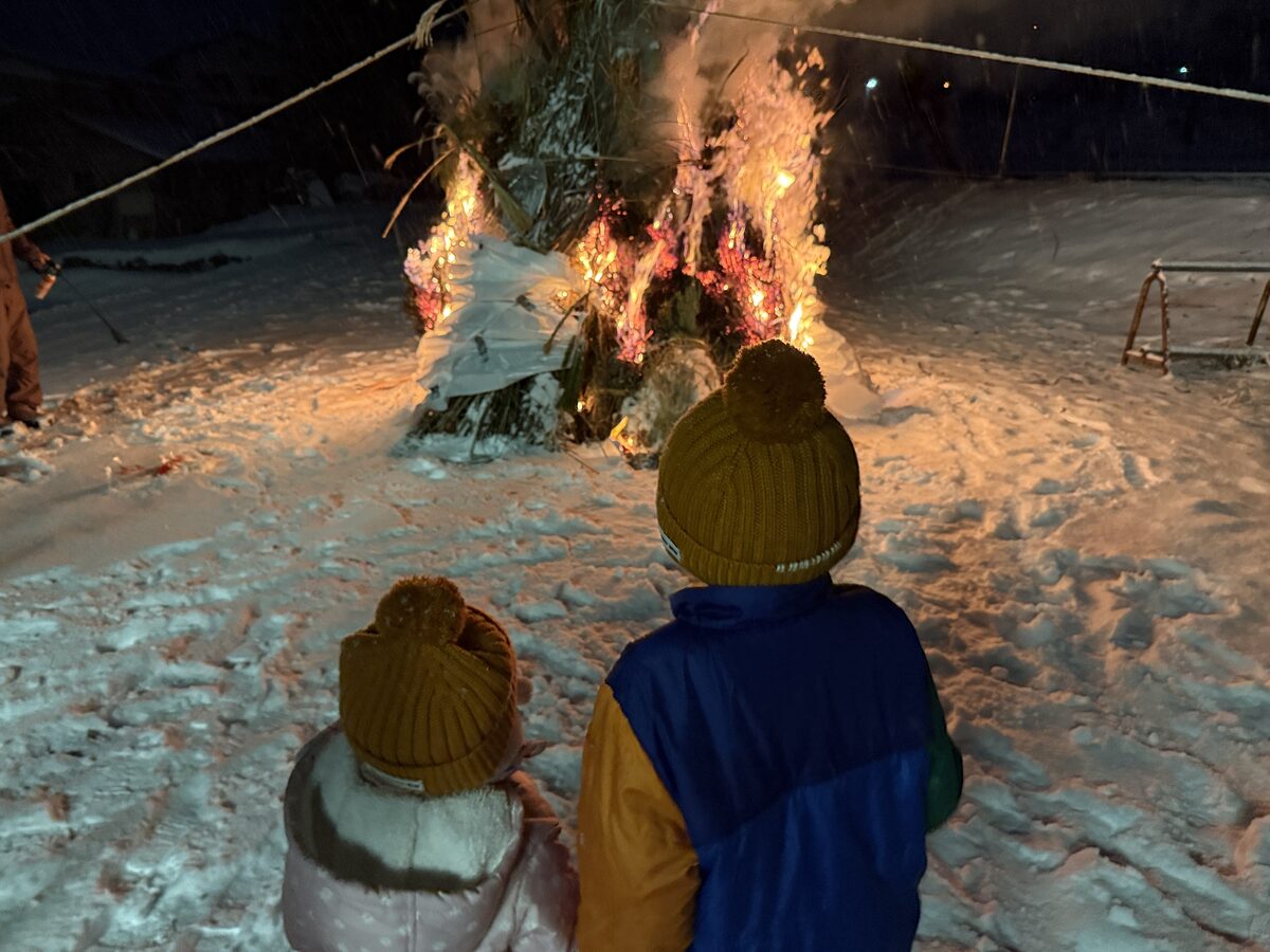 雪の中で燃えるどんど焼きの櫓と、それを見つめる子どもたち